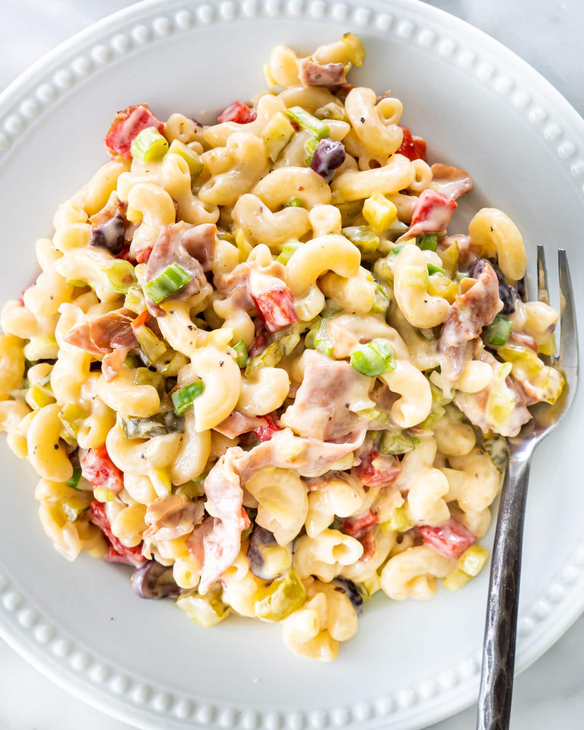 overhead shot of macaroni salad with prosciutto in a white plat with a fork