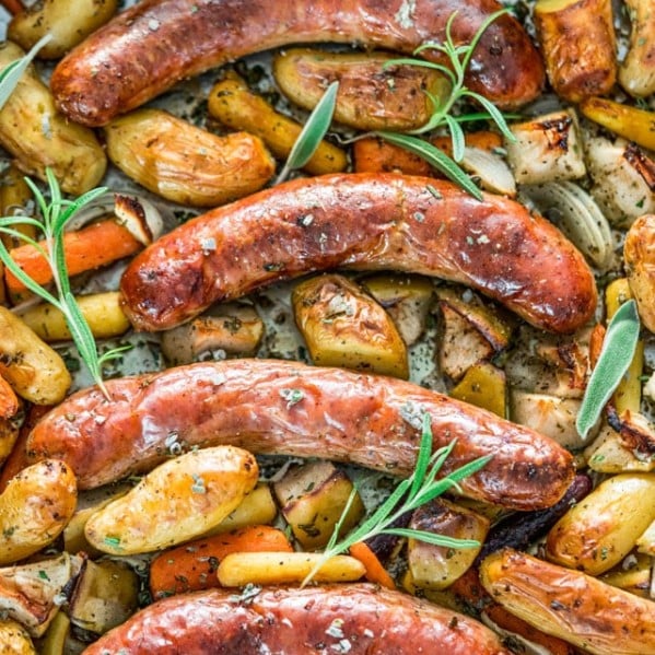 overhead shot of baked sausages with apples, potatoes and herbs on a baking sheet