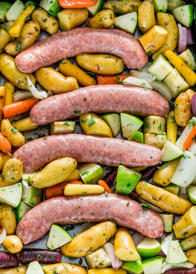 Baked Sausages with Apples, potatoes, and carrots, on a pan ready to go into the oven