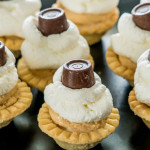 side view close up shot of peanut butter pie mini tarts topped with whipped cream and rolos
