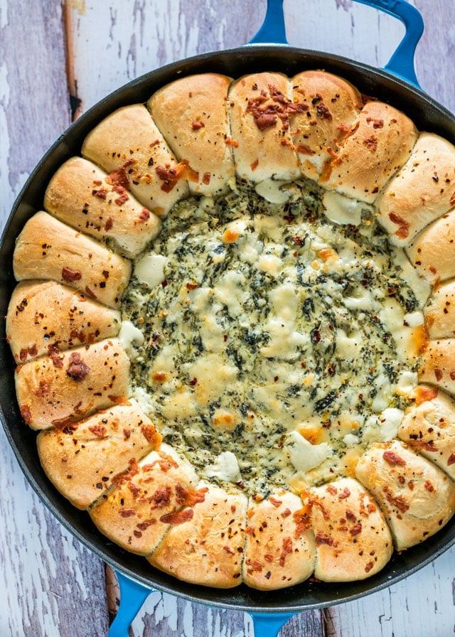 overhead of a pan of Spinach and Artichoke Dip with a ring of bread rolls