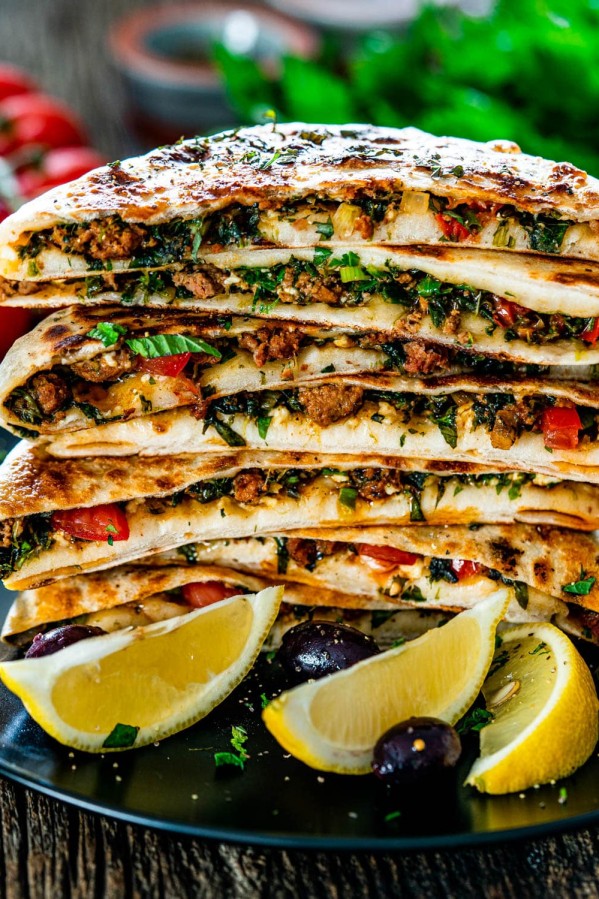 a stack of turkish gozleme on a plate with lemon wedges and olives as garnish