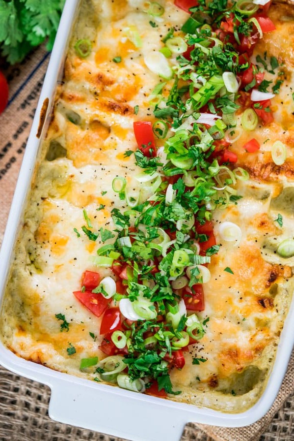 overhead shot of the green chile chicken enchilada casserole in a baking dish topped with diced tomato and green onion