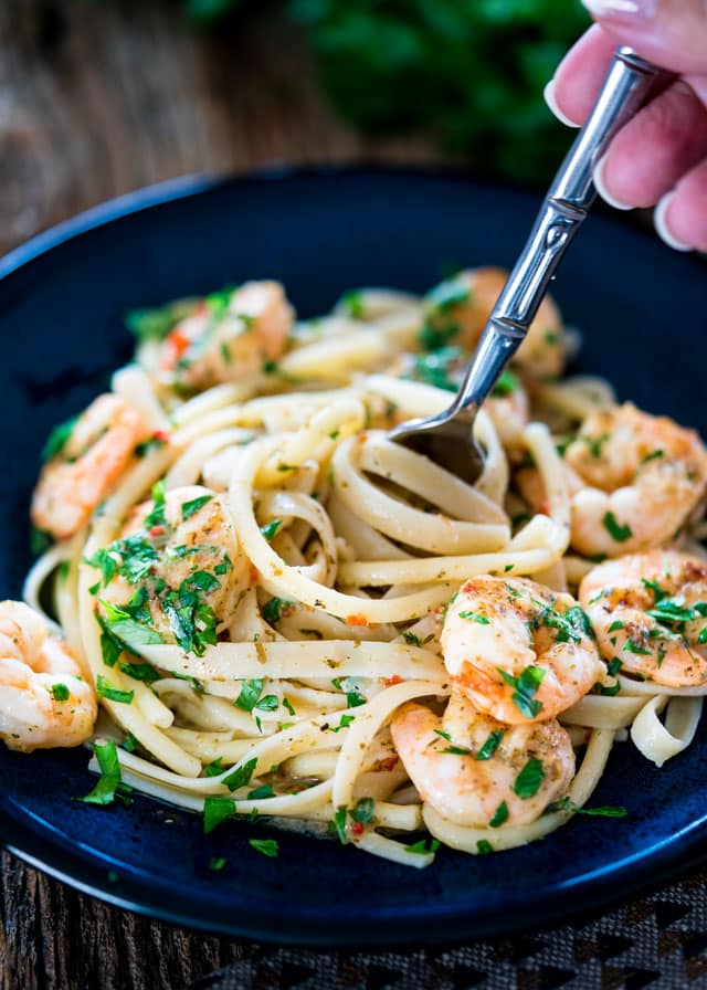 a fork twirling fettuccine on a plate with shrimp and parsley
