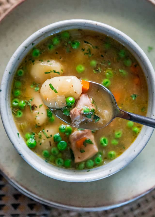 overhead of a spoon scooping gnocchi, chicken, peas, and broth over a bowl full of soup
