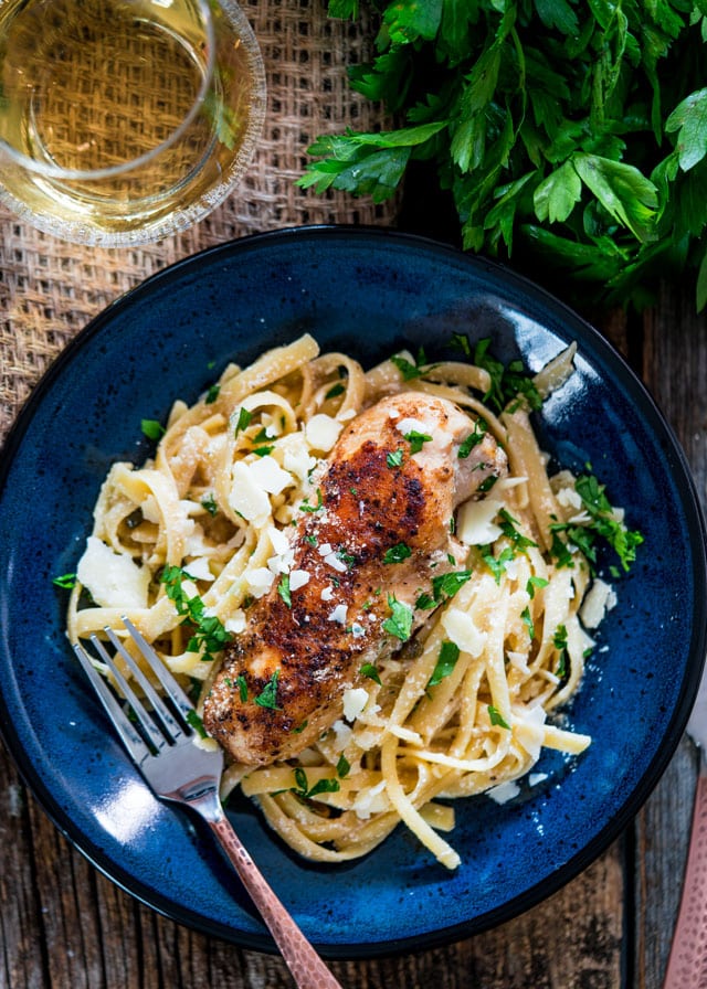 overhead of a plate with fettuccine, chicken breast, topped with parmesan cheese and parsley