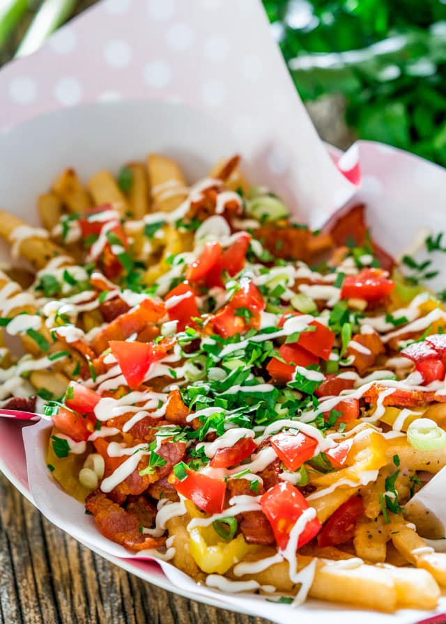 a basket of fries topped with tomatoes, parsley, mayo, and bacon