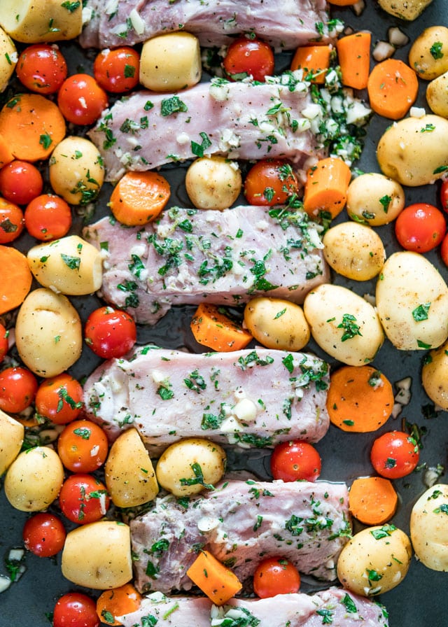 overhead of a sheet pan filled with potatoes, cherry tomatoes, carrots, and pork loin before going into the oven