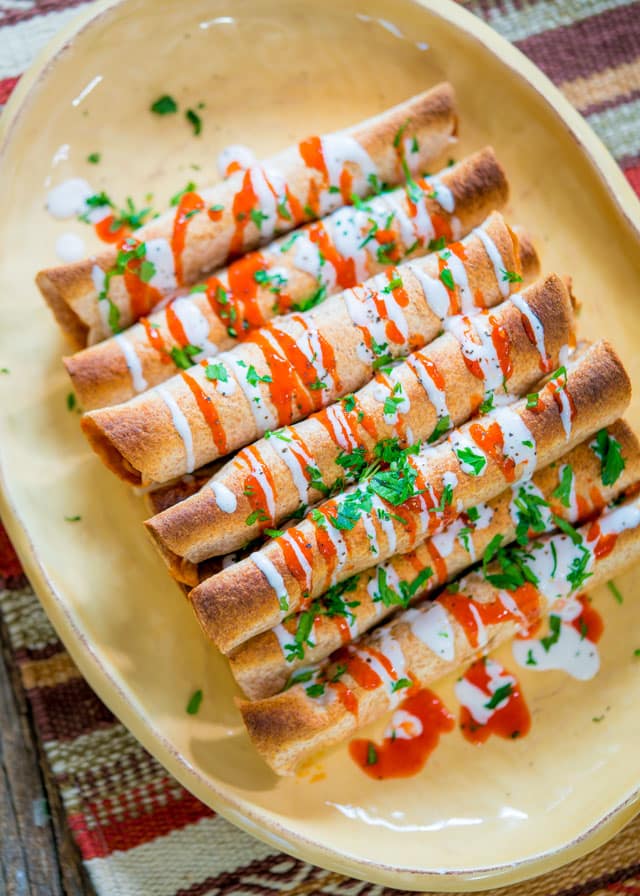7 taquitos lines up on a platter drizzled with creme fraiche and hot sauce