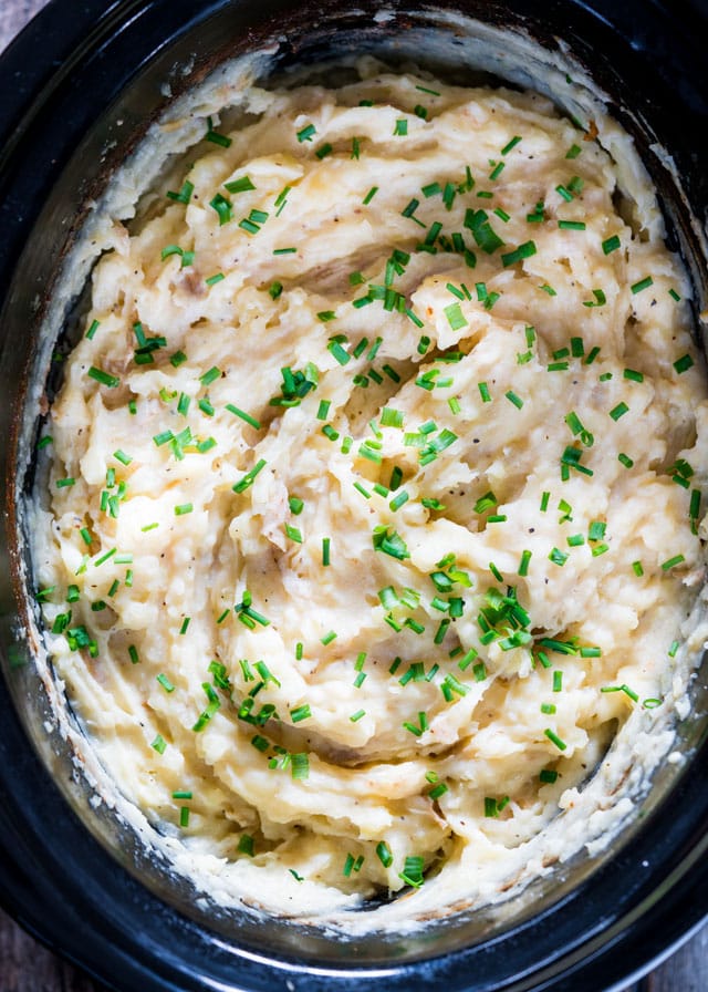 overhead of a crockpot filled with mashed potatoes garnished with chives