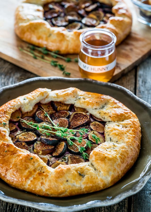 a plate with a galette filled with figs, garnished with sprigs of thyme, and a jar of honey in the background.
