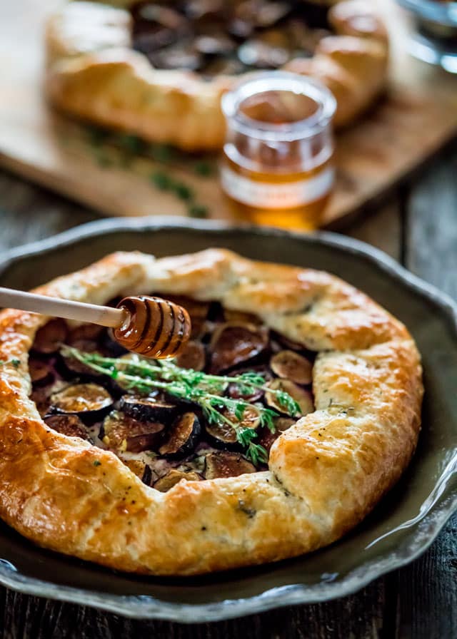 a plate with a galette filled with figs, garnished with thyme sprigs and a honey comb drizzling honey over it.