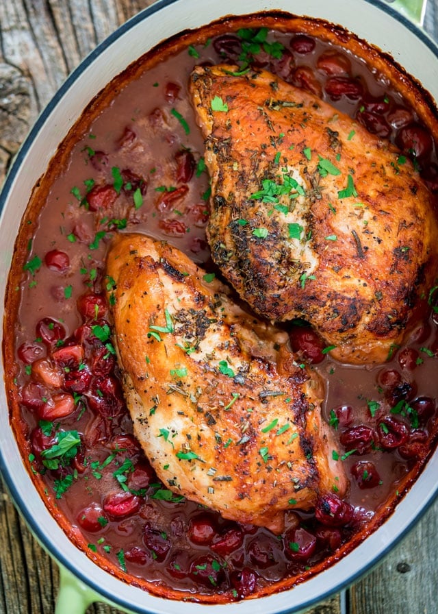 overhead of a large pot with 2 roasted turkey breasts sitting in lots of cranberry sauce