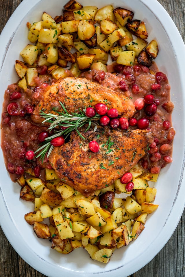 2 turkey breasts on a platter with cranberry sauce, roasted potatoes, and fresh rosemary