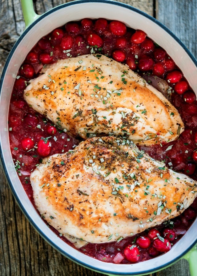2 turkey breasts topped with herbs sitting on fresh cranberries in a large pot