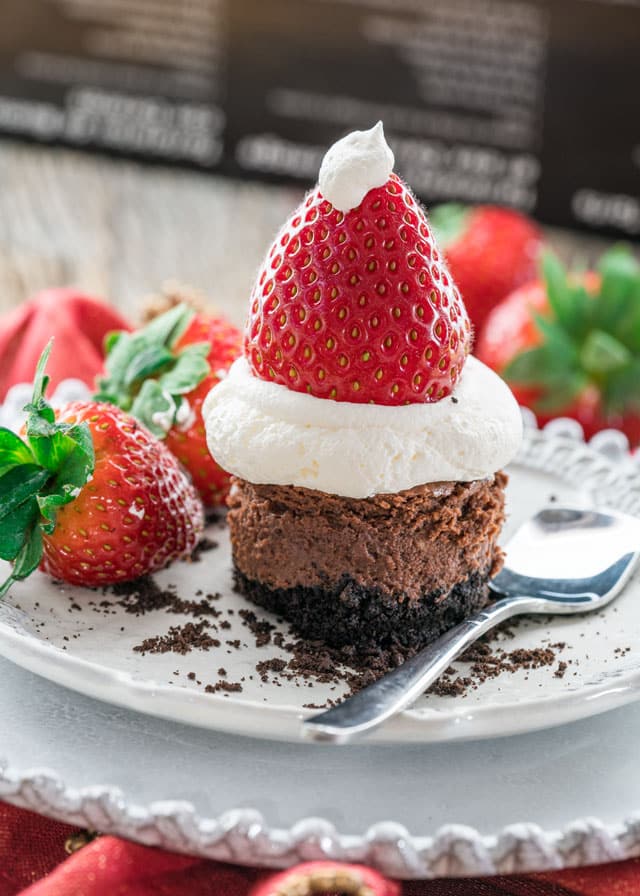 a mini chocolate cheesecake topped with a whipped cream and strawberry santa hat