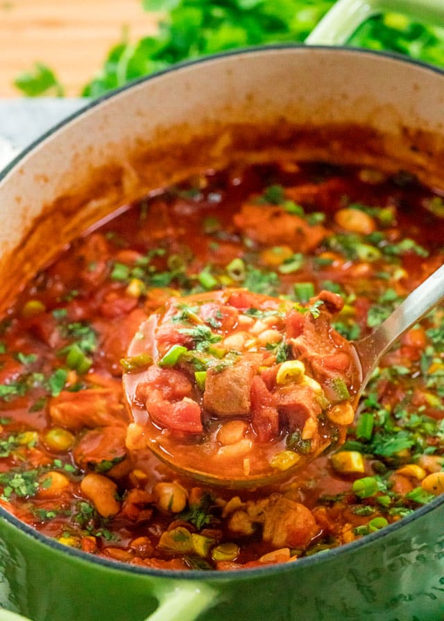 a green put filled with pork stew with corn, tomatoes, and parsley