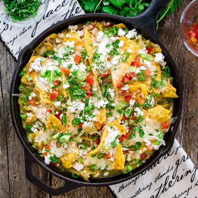 overhead of a skillet filled with chilaquiles and topped with queso fresco, tomatoes, parsley, and scallions