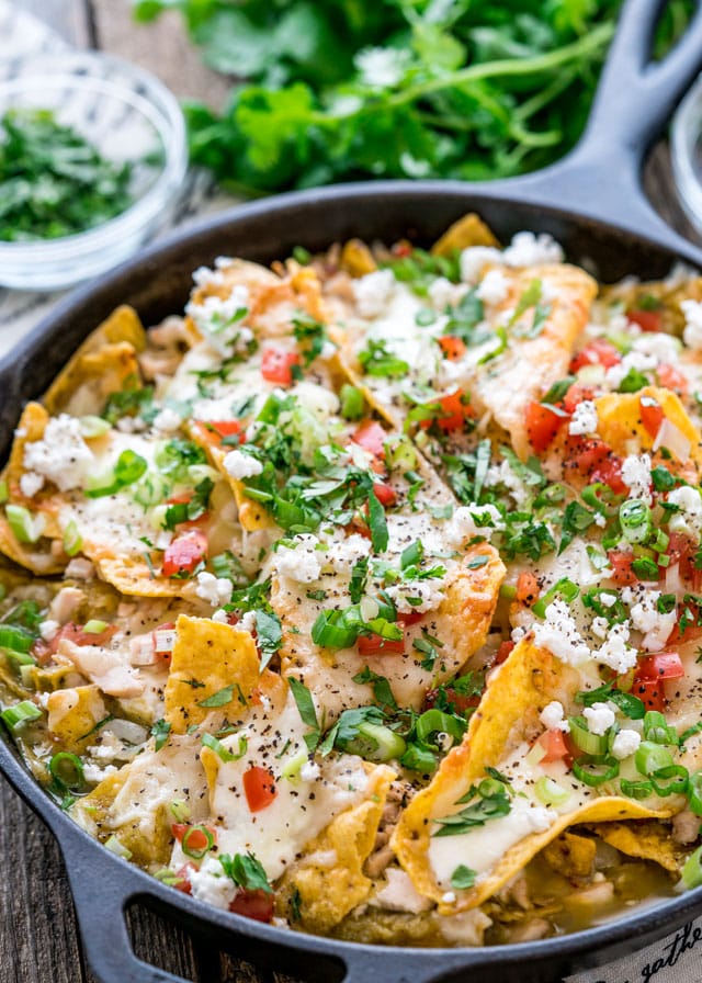 a skillet filled with chilaquiles and topped with queso fresco, parsley, parsley, and scallions