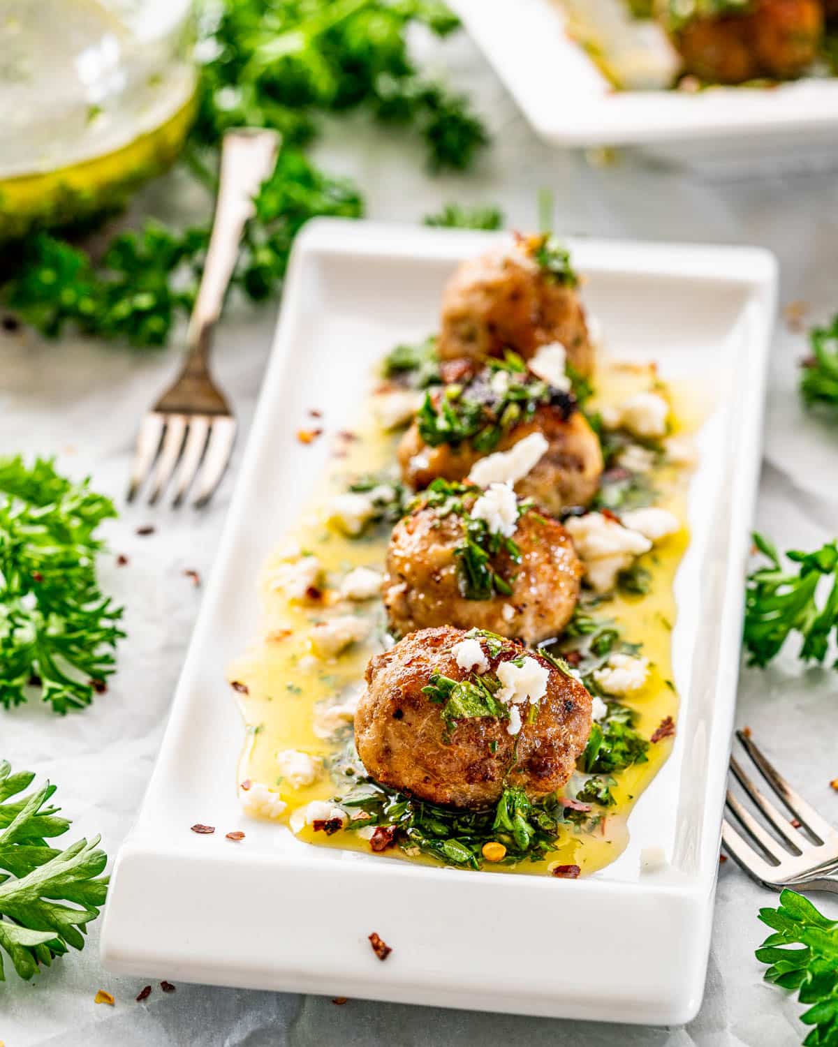 a long white plate with 4 chimichurri meatballs garnished with feta cheese