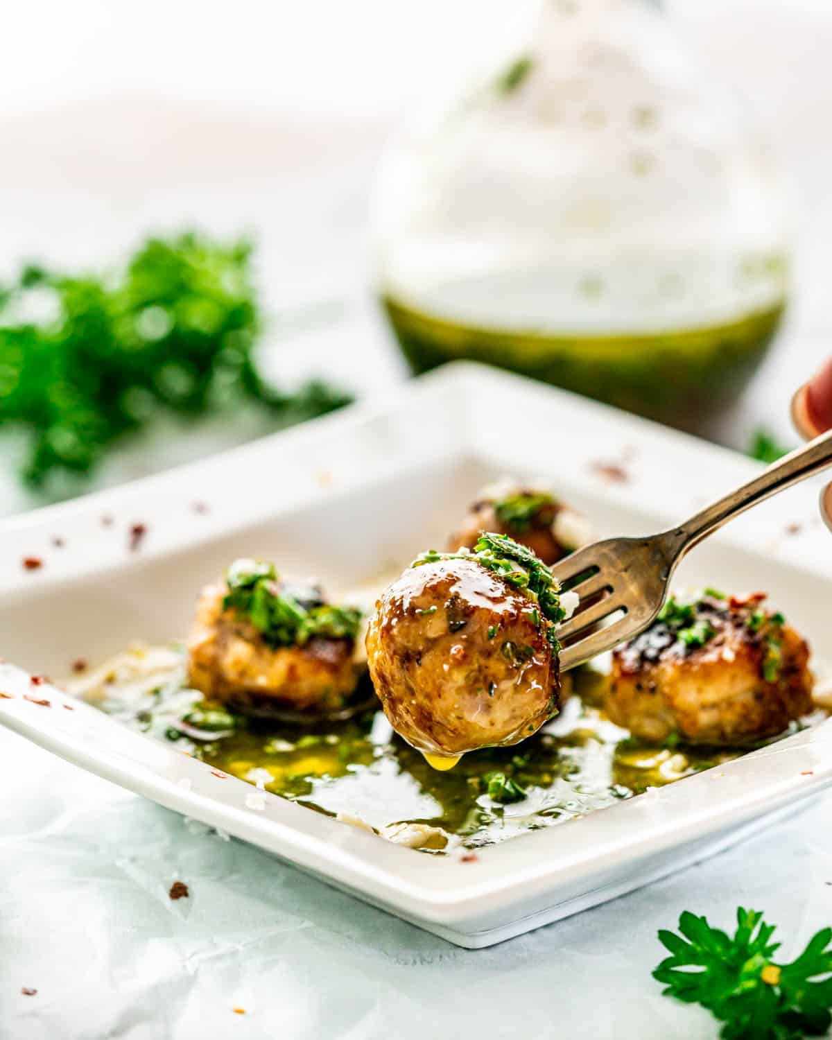 a fork holding a meatball over a plate of chimichurri meatballs