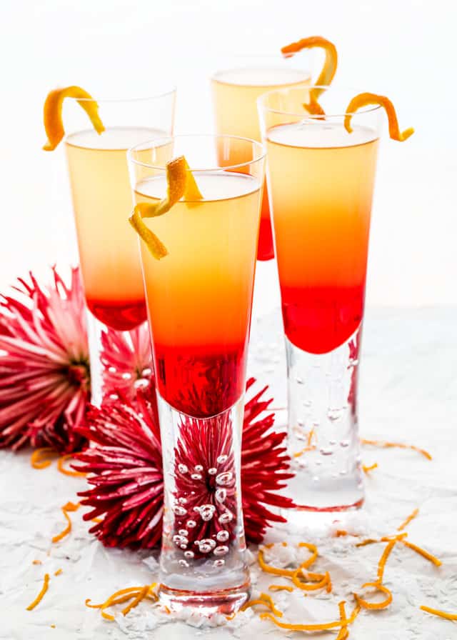 four glasses of grenadine sunrise with twists of orange and flowers