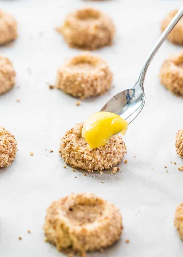 using a teaspoon to scoop lemon curd into a thumbprint cookie