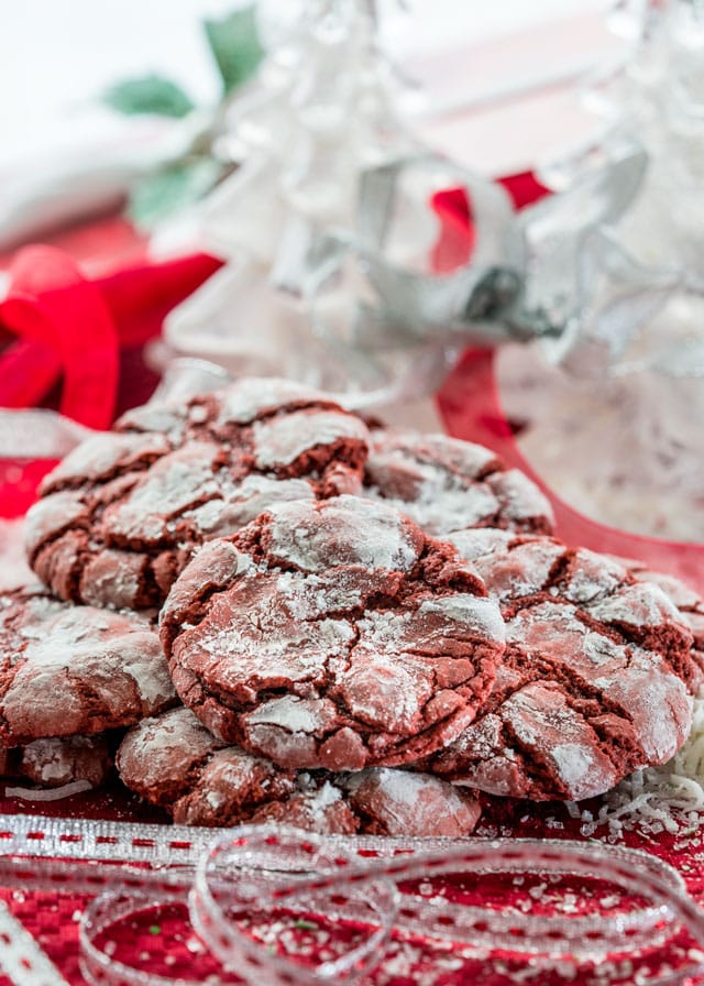 a pile of red velvet crinkle cookies with christmas decorations in the background