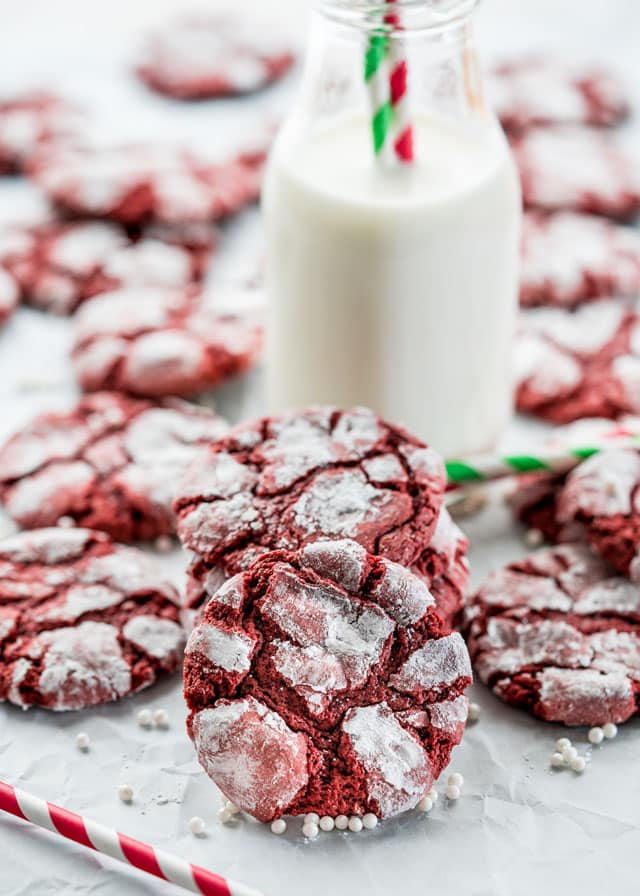 a pile of red velvet crinkle cookies with a class of milk in the background