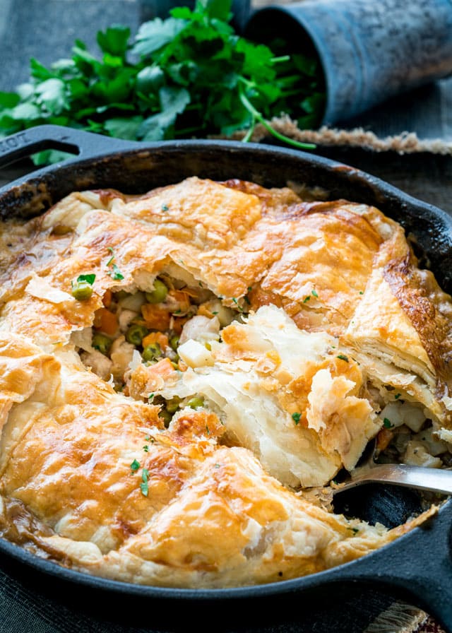 a large spoon scooping a portion from a skillet filled with pot pie topped with flaky pastry