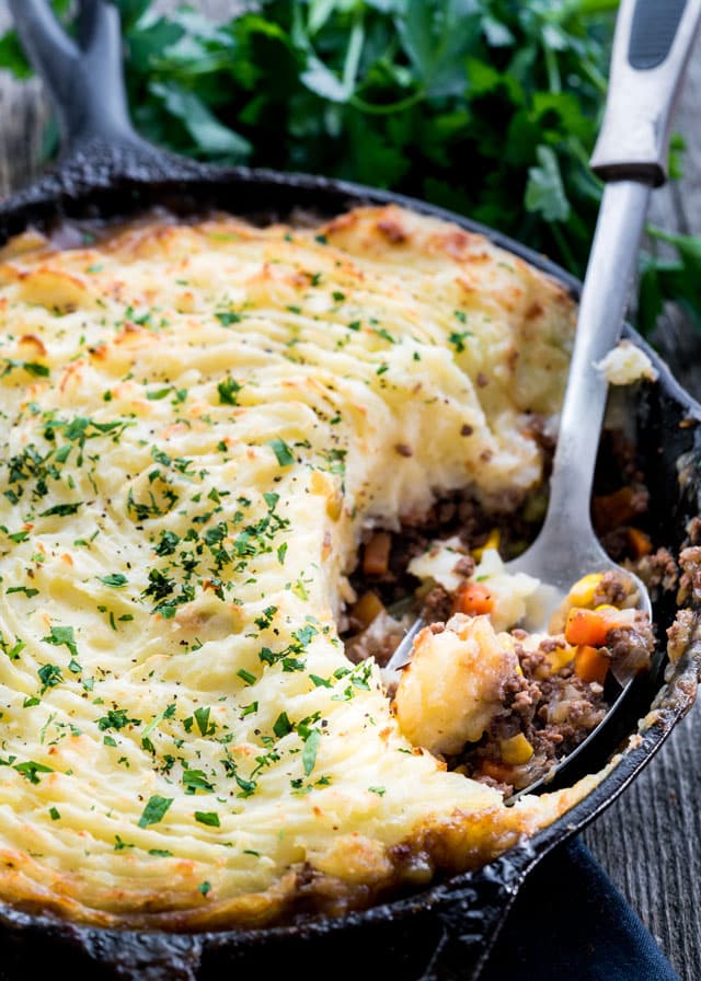 a spoon taking a big scoop out of a skillet full of shepherd's pie