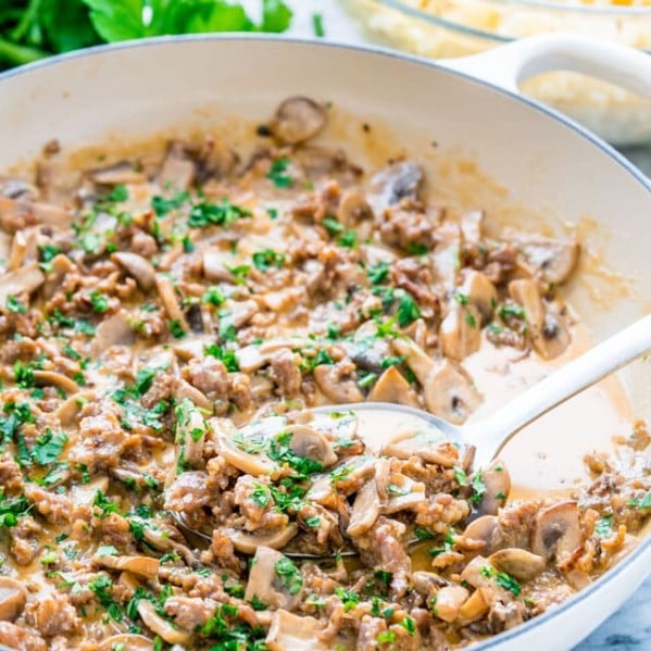 side view shot of a serving spoon taking a scoop of creamy sausage and mushrooms from a pan