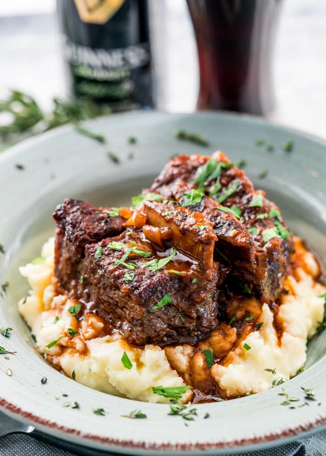 a bowl of braised short ribs over mashed potatoes topped with parsley with a can of guinness in the background