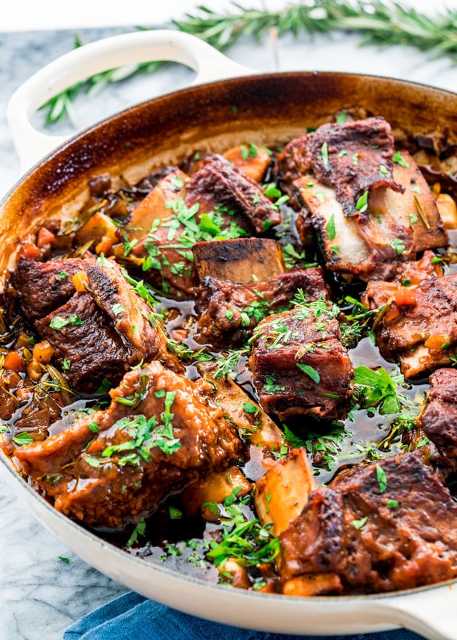 a braiser filled with braised short ribs in a dark sauce topped with parsley