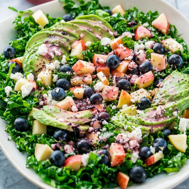 a kale salad loaded with avocado, apples blueberries, and feta.