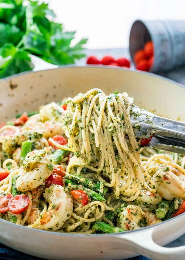 a braiser full of pasto with pesto, prawns, asparagus, and cherry tomatoes.