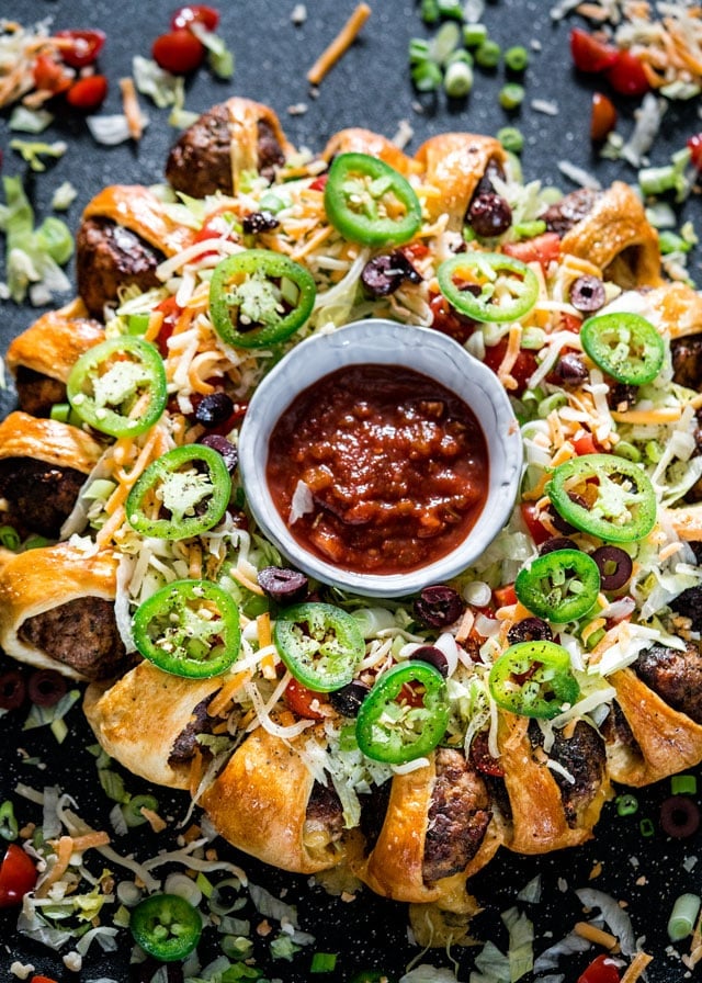 overhead of a taco meatball ring covered in toppings with a bowl of salsa in the middle