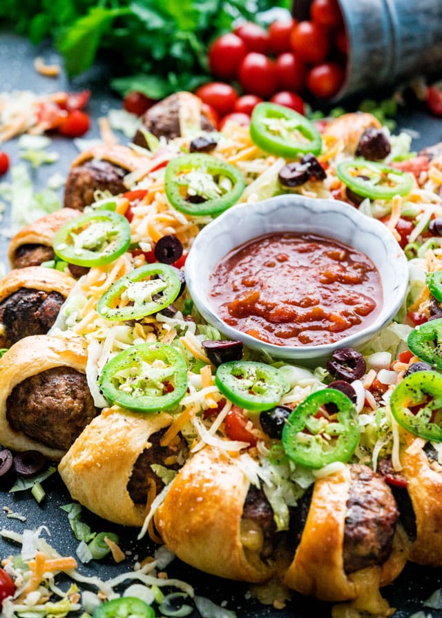 a meatball ring covered in taco toppings with a bowl of salsa in the middle