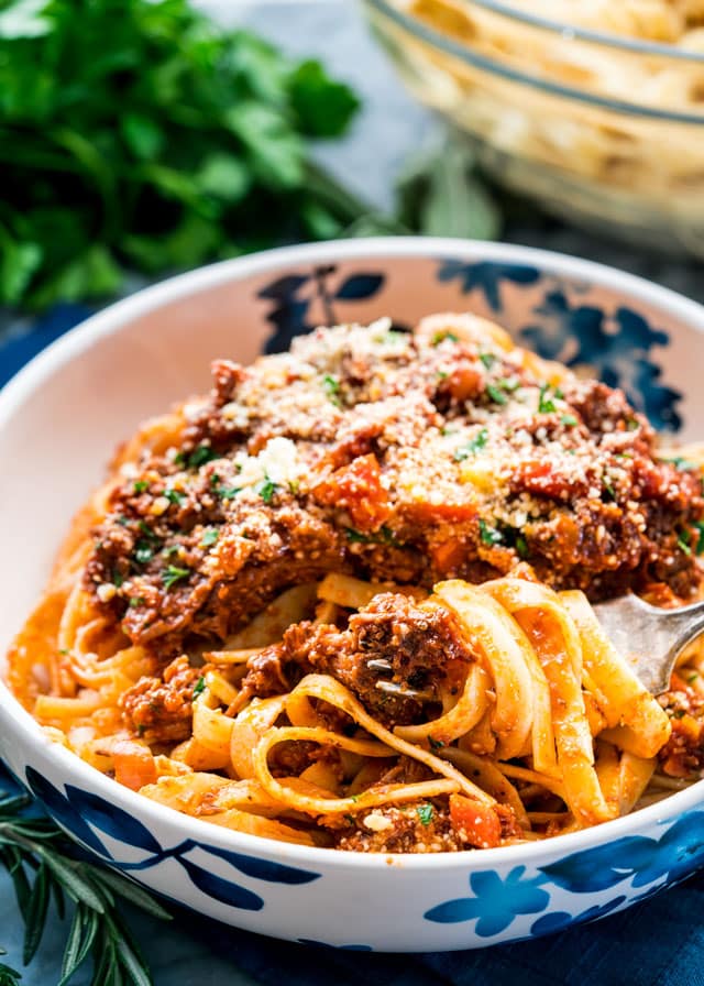 a bowl full of ragu topped with parmesan with fettuccini twirled around a fowk