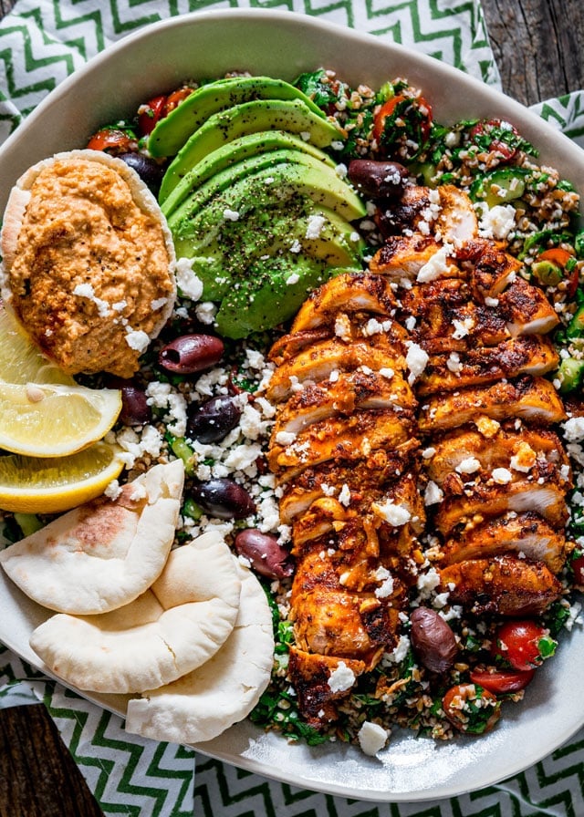 overhead of a salad loaded with pita, hummus, lemon wedges, avocado, chicken shawarma, and olives.