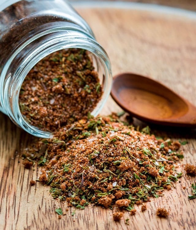 a jar of jamaican jerk seasoning laying on its side with seasoning spilling out