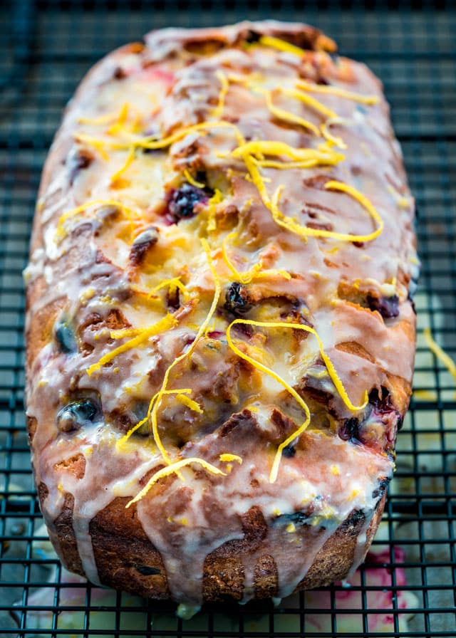 a lemon blueberry loaf on a cooling rack doused in glazed and topped with lemon zest