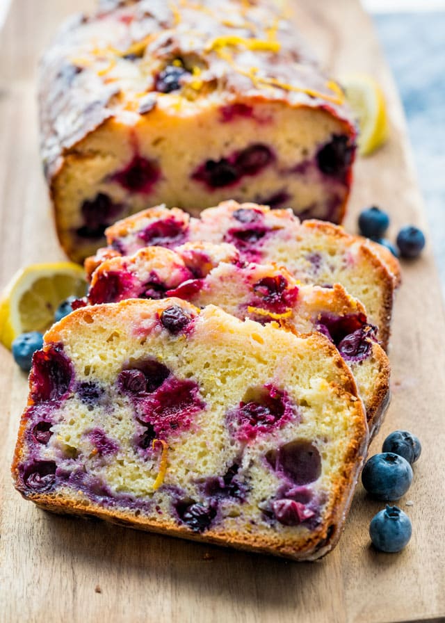 lemon blueberry loaf on a cutting board with 3 slices cut surrounded by blueberries