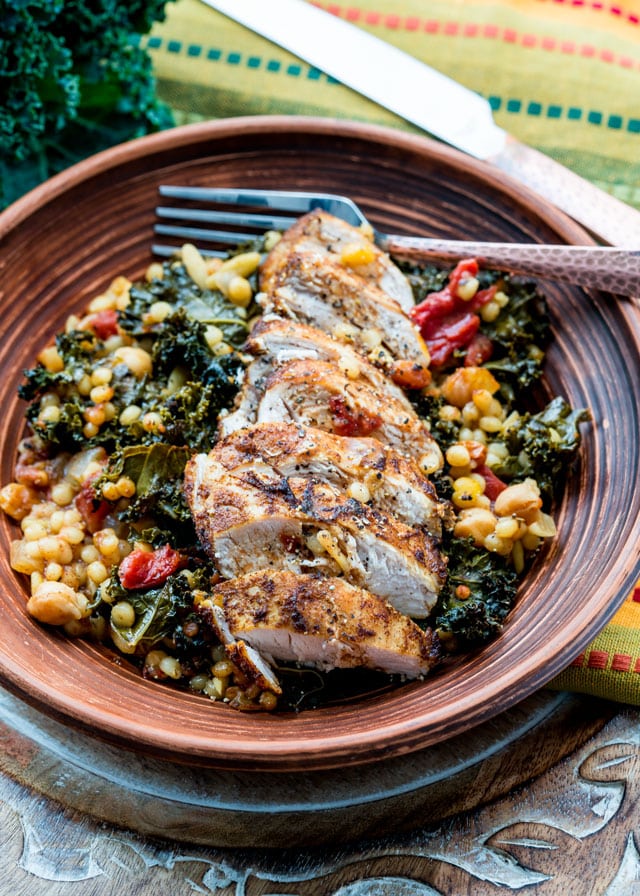 a plate of couscous with kale, topped with a sliced chicken breast with a fork