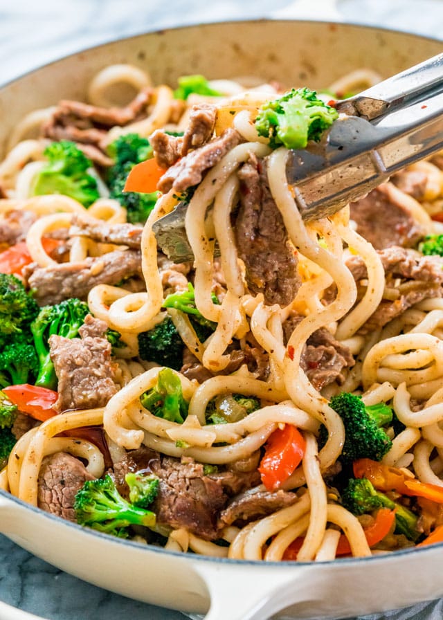 a pair of tongs holding noodles with beef and broccoli