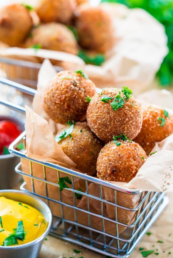 side view shot of a metal fry basket full of bitterballen with a side of mustard