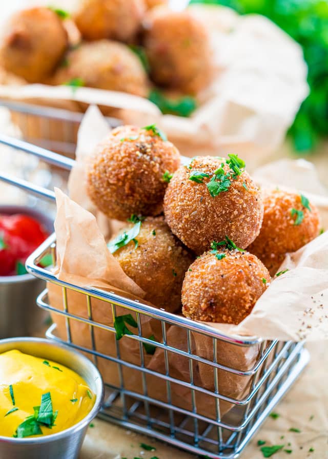 side view shot of a metal fry basket full of bitterballen with a side of mustard