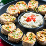side view shot of a plate of cheesy chicken roll ups with a bowl of dip in the center