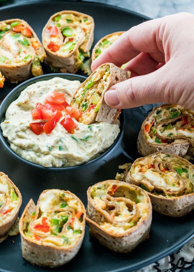 Cheesy Chicken Veggie Rollups on a plate, one being dipped into a creamy dip