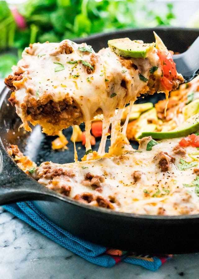 a spatula lifting a cheesy beef tamale out of a skillet